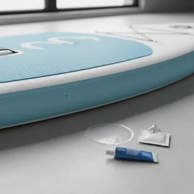 Overview of an inflatable paddle board with a small puncture, highlighting the PVC material and a repair kit nearby
